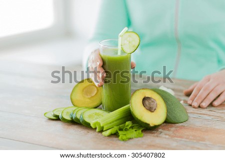 healthy eating, food, dieting and people concept - close up of woman hands with green fresh juice and vegetables sitting at table