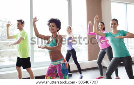 fitness, sport, dance and lifestyle concept - group of smiling people with coach dancing zumba in gym or studio