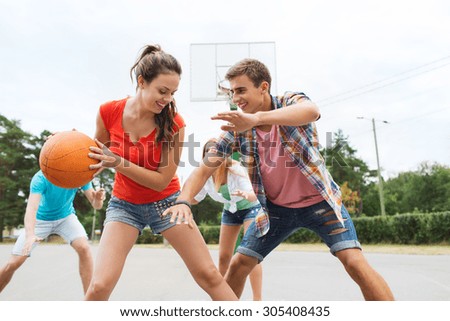 summer vacation, sport, games and friendship concept - group of happy teenagers playing basketball outdoors