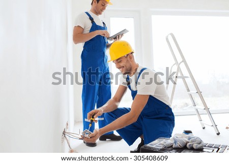 building, renovation, technology, electricity and people concept - two builders with tablet pc computer fixing wiring indoors