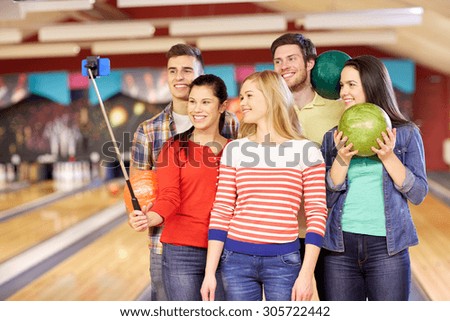people, leisure, sport, friendship and entertainment concept - happy friends taking selfie with smartphone on monopod in bowling club