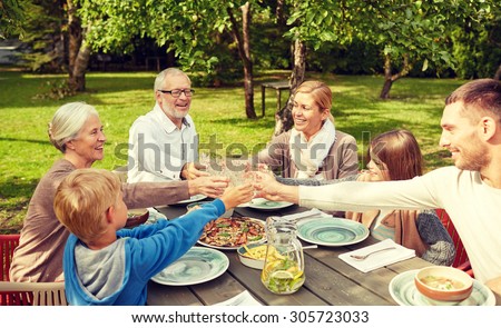 family, generation, home, holidays and people concept - happy family having dinner and clinking glasses in summer garden