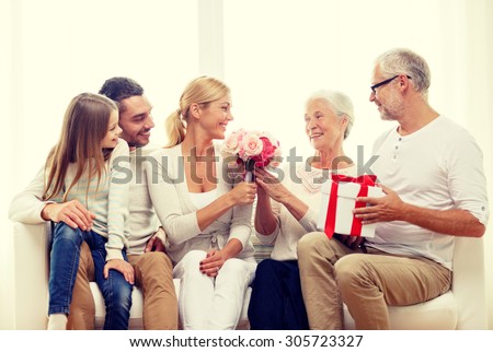 family, happiness, generation, holidays and people concept - happy family with bunch of flowers and gift box sitting on couch at home