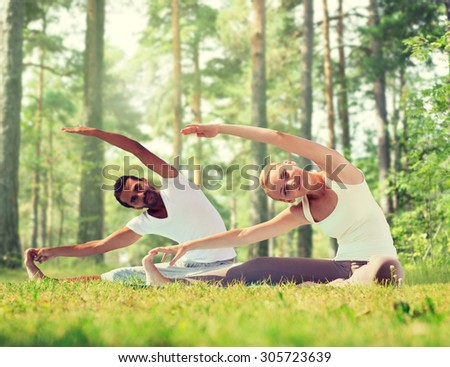fitness, sport, yoga and people concept - happy couple stretching on mats over green woods background