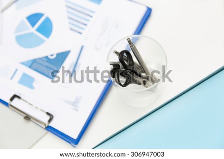 business, stationery and office supply concept - close up of organizer with scissors and pens over charts on table