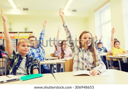 education, elementary school, learning and people concept - group of school kids with notebooks sitting in classroom and raising hands