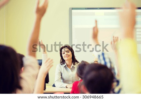 education, elementary school, learning and people concept - group of school kids with teacher sitting in classroom and raising hands
