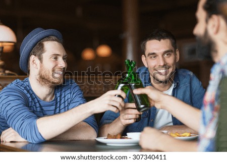 people, leisure, celebration, friendship and bachelor party concept - happy male friends drinking beer and clinking bottles at bar or pub