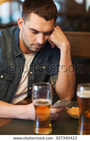 people and technology concept - man with smartphone drinking beer and reading message at bar