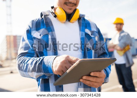 building, technology and people concept - close up of smiling builder with headphones and tablet pc computer outdoors