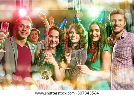 party, holidays, celebration, nightlife and people concept - smiling friends in party caps with glasses of champagne in club