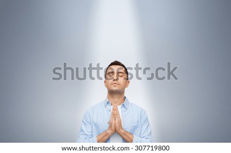 faith in god, religion and people concept - happy man with closed eyes praying under ray of ligh over gray background