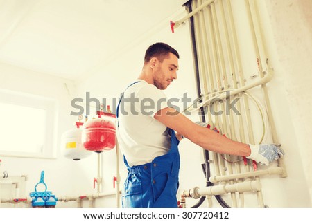 building, profession and people concept - builder or plumber working with water pipes in boiler room