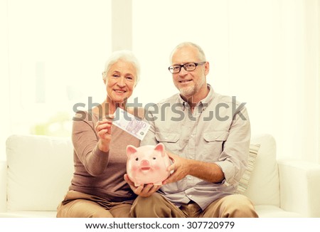 family, savings, age and people concept - smiling senior couple with money and piggy bank at home