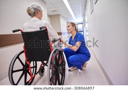 medicine, age, support, health care and people concept - happy nurse talking to senior woman patient in wheelchair at hospital corridor