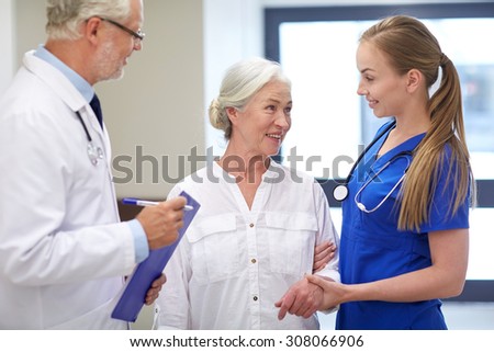 medicine, age, health care and people concept - male doctor with clipboard, young nurse and senior woman patient talking at hospital corridor