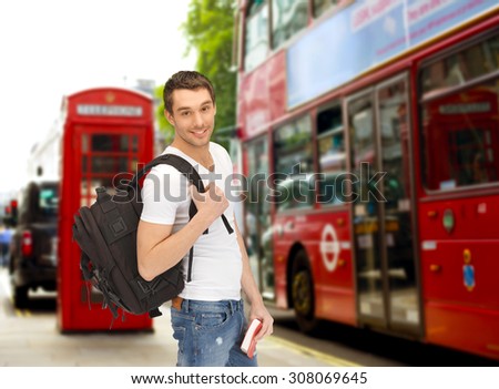 people, travel, tourism and education concept - happy young man with backpack and book over london city bus on street background