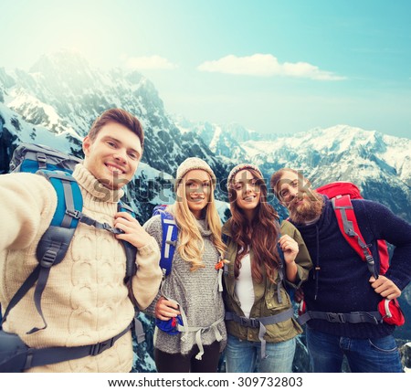 adventure, travel, tourism, hike and people concept - group of smiling friends with backpacks making selfie over alpine mountains background