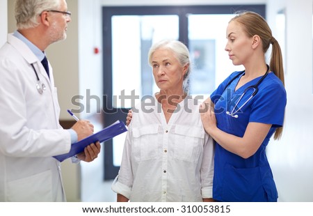 medicine, age, health care and people concept - male doktor with clipboard, young nurse and senior woman patient talking at hospital corridor