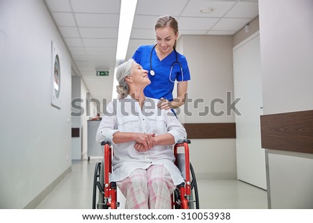 medicine, age, support, health care and people concept - happy nurse taking senior woman patient in wheelchair at hospital corridor