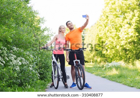 fitness, sport, people, technology and healthy lifestyle concept - happy couple with bicycle taking selfie by smartphone outdoors