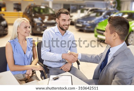 auto business, car sale, and people concept - happy couple with dealer shaking hands in auto show or salon