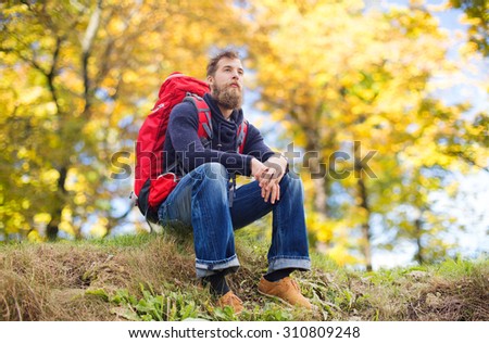 adventure, travel, tourism, hike and people concept - smiling man with red backpack sitting on ground over natural background