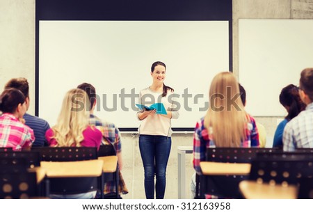 education, high school, teamwork and people concept - smiling student girl with notebook standing in front of students in classroom