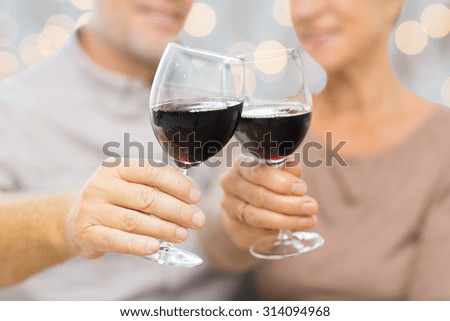 family, holidays, drinks, age and people concept - close up of happy senior couple clinking glasses with red wine over lights background