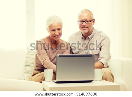 family, technology, drinks, age and people concept - happy senior couple with laptop computer and cups at home