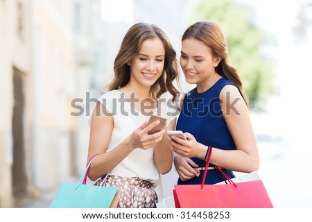 sale, consumerism and people concept - happy young women with shopping bags and smartphone on city street