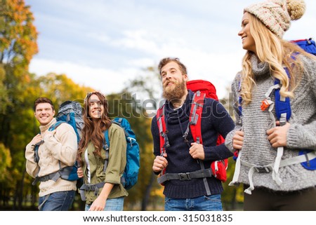 adventure, travel, tourism, hike and people concept - smiling friends walking with backpacks over natural background
