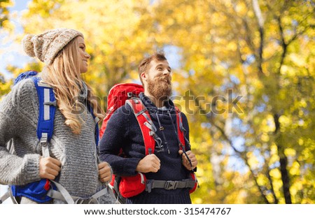 adventure, travel, tourism, hike and people concept - smiling couple walking with backpacks over autumn natural background