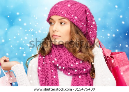 holidays, christmas, sale and people concept - young woman in winter clothes with shopping bags over blue snowy background