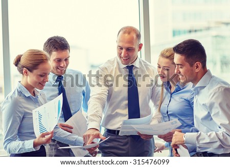 business, teamwork, people and technology concept - smiling business team with papers meeting and talking in office