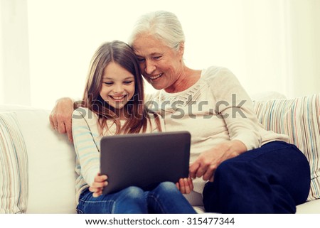family, generation, technology and people concept - smiling granddaughter and grandmother with tablet pc computer sitting on couch at home