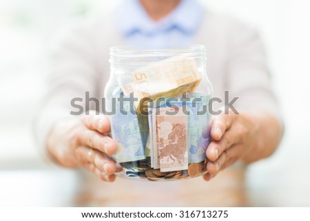 savings, money, annuity insurance, retirement and people concept - close up of senior woman hands holding money in glass jar