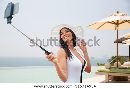 travel, leisure, summer, technology and people concept - sexy young woman taking selfie with smartphone over hotel resort infinity edge pool or beach background