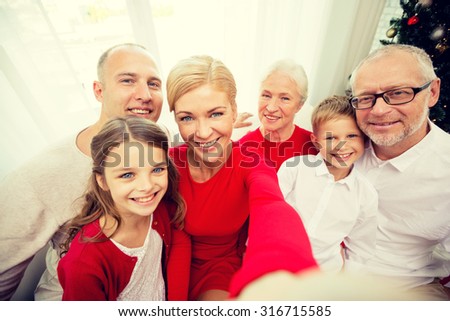 family, holidays, generation, christmas and people concept - smiling family with camera or smartphone making selfie at home