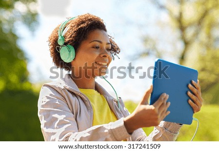 technology, lifestyle and people concept - smiling african american young woman or teenage girl with tablet pc computer and headphones listening to music or watching video in summer park