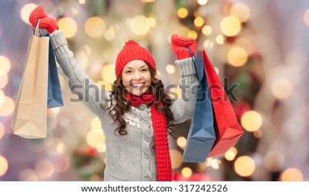 holidays, x-mas, sale and people concept - happy young asian woman in winter clothes with shopping bags over christmas tree lights background