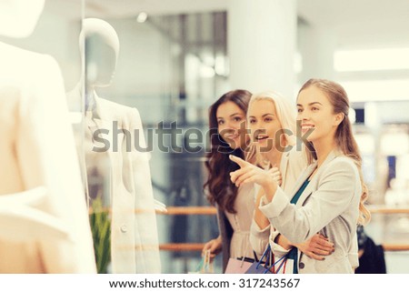 sale, consumerism and people concept - happy young women with shopping bags pointing finger to shop window in mall