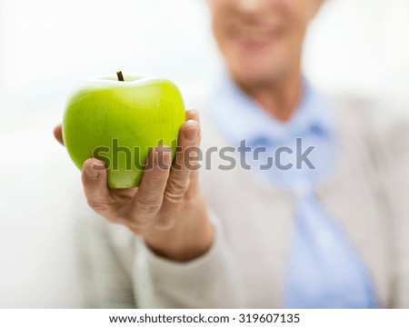 age, healthy eating, food, diet and people concept - close up of happy smiling senior woman with green apple at home