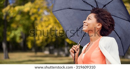 business, weather, season, fall and people concept - young smiling african american woman with umbrella over autumn park background