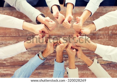 business, people, gesture and team work concept - close up of creative team showing thumbs up and sitting at table in office