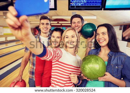people, leisure, sport, friendship and entertainment concept - happy friends taking selfie with smartphone in bowling club