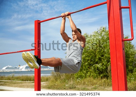 fitness, sport, exercising, training and lifestyle concept - young man doing abdominal exercise on horizontal bar in summer park