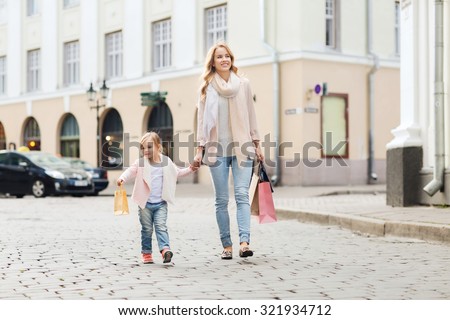 sale, consumerism and people concept - happy mother and child with shopping bags walking along city street
