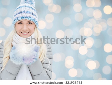 season, christmas, holidays and people concept - smiling young woman in winter clothes over lights background