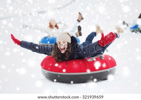 winter, leisure, sport, friendship and people concept - group of happy friends sliding down on snow tubes
